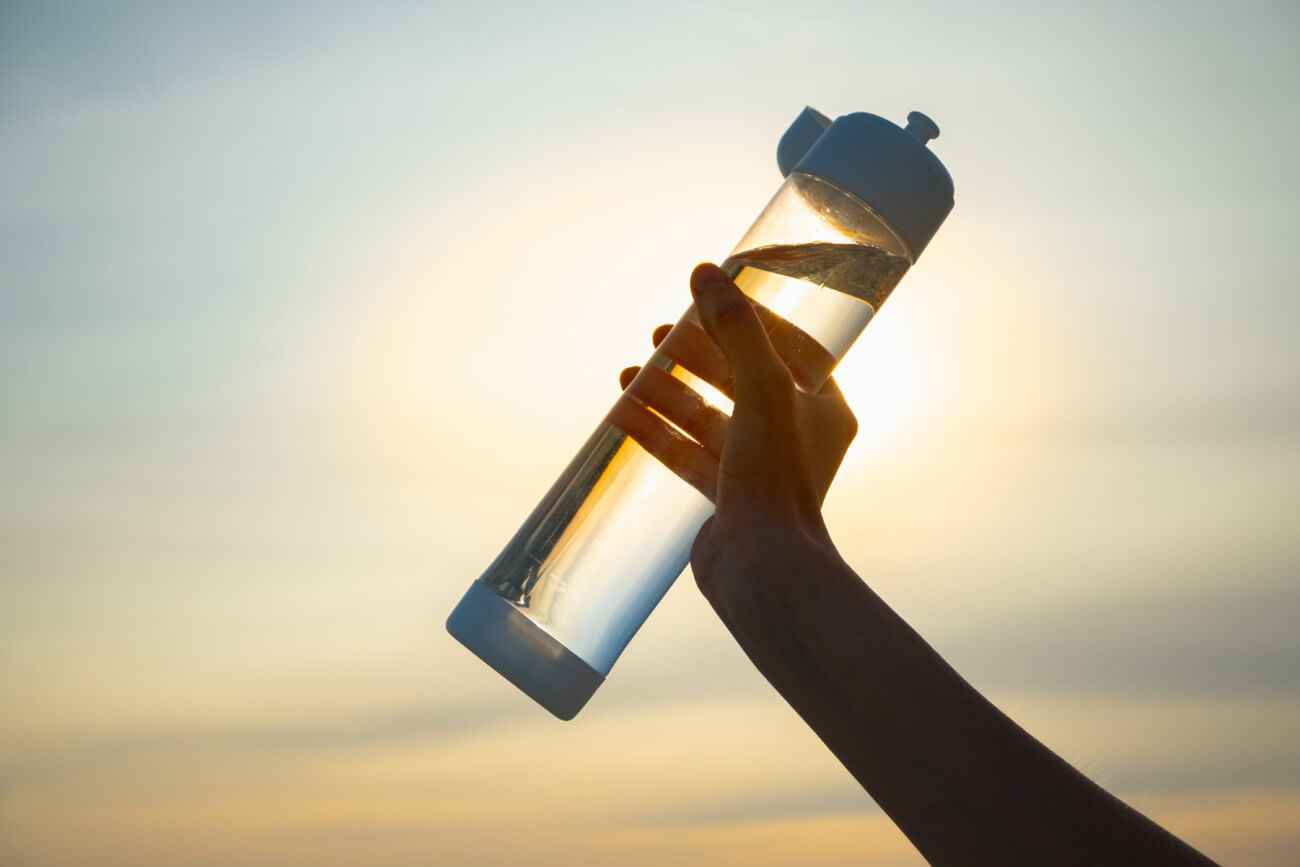 Mano humana sosteniendo una botella de agua contra el sol poniente