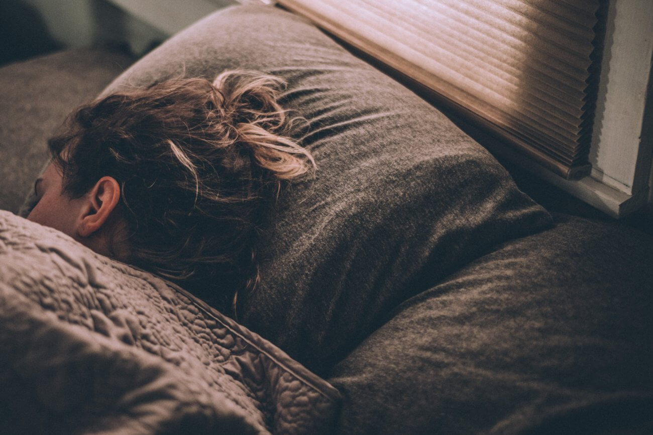 mujer morena durmiendo bajo las cubiertas de la cama con la cabeza sobre una almohada